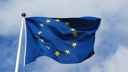 EU flag on flagpole, fluttering in breeze, against a cloudy sky