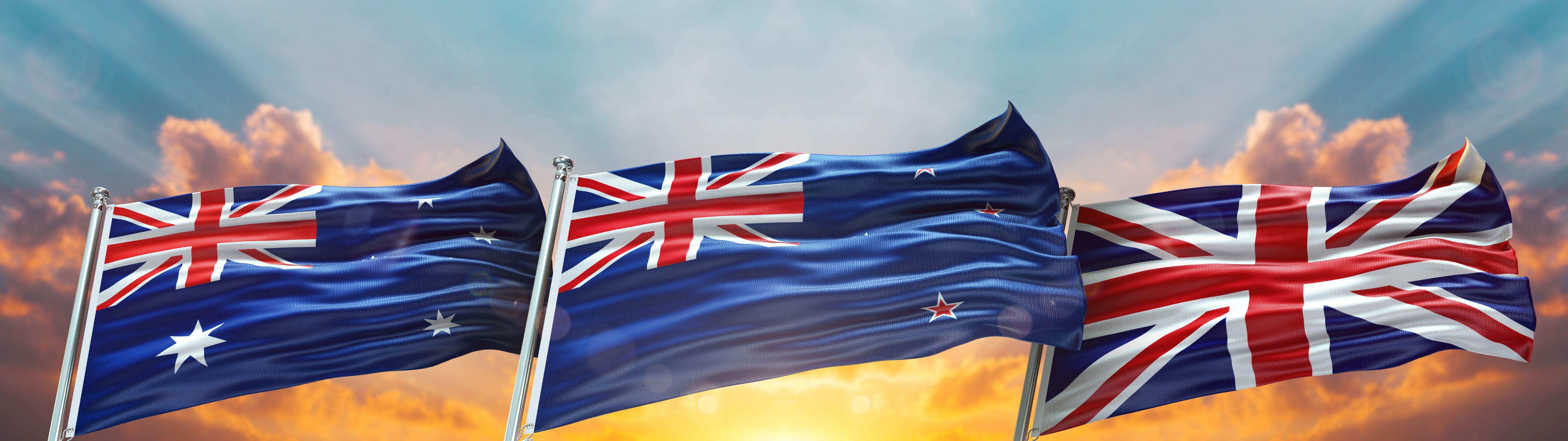 UK Australia and New Zealand flags hanging on flag pole with sunset in background