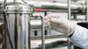 Gloved hand holds test tube in front of machinery