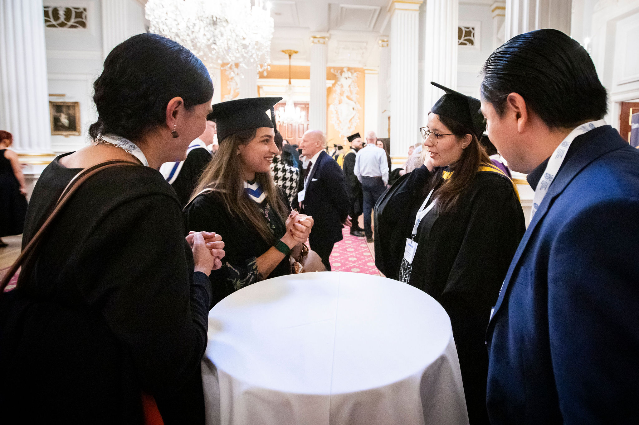 Image of individuals in graduation hats and gowns standing around table