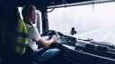 Lorry driver sitting in front of steering wheel, driving large truck along a motorway