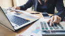 Woman working at laptop with a calculator, conducting an audit at her desk